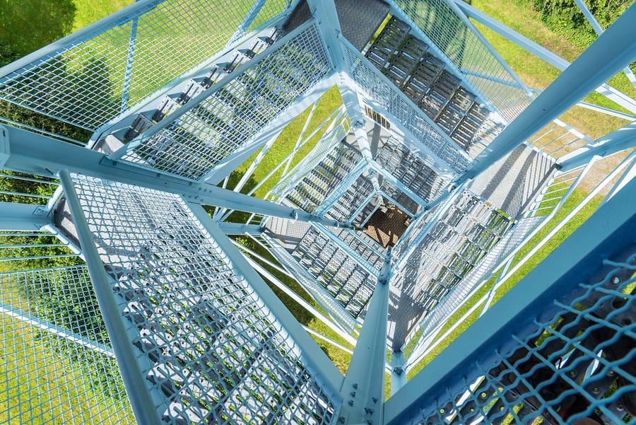 View from above through the open stairway of a light blue metal tower