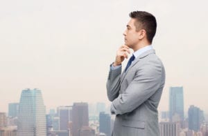 business and people concept - thinking businessman in suit making decision over city background
